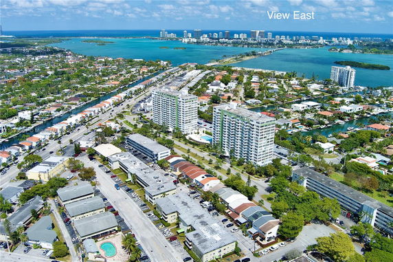 Aerial view showing a cityscape with multiple buildings and a vast body of water in the background.