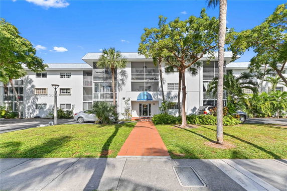 Front view of a three-story apartment building with balconies and a striped canopy over the entrance.