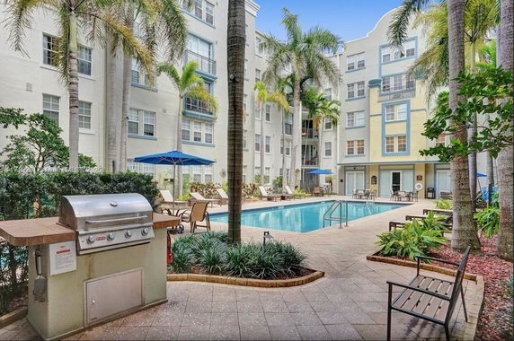 Outdoor swimming pool area surrounded by a multi-story building, with lounge chairs and a barbecue grill.