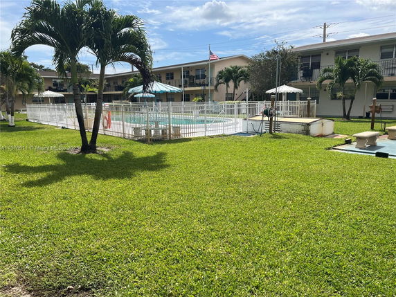 Outdoor swimming pool area with surrounding white fence and adjacent buildings.