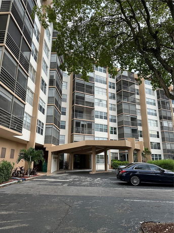 Front view of a multi-story residential building with a covered entrance and parking area.