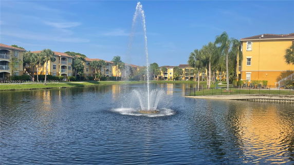View of several yellow multi-story buildings surrounding a pond with a central fountain.