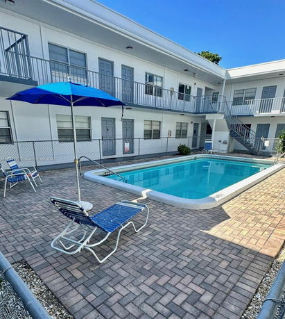 Outdoor swimming pool area of a two-story building with patio chairs and umbrellas.