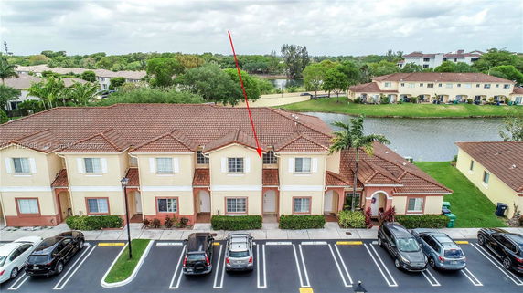 Aerial view of a row of two-story townhouses with a parking lot in front, adjacent to a body of water.