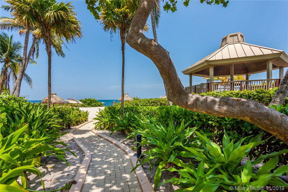 Pathway leading to a beach with palm trees and a gazebo on the right.