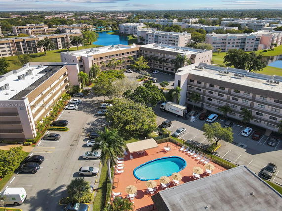 Aerial view of a residential complex with multiple multi-story buildings, parking spaces, and a swimming pool.