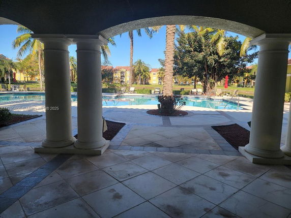 View of a swimming pool area with surrounding greenery and columns.