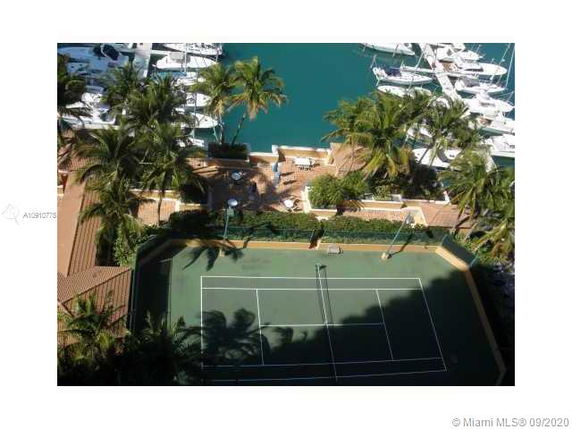 Aerial view of a tennis court adjacent to a marina with multiple boats docked.
