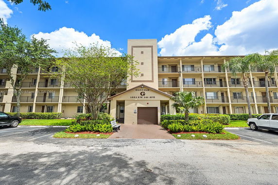Front view of a multi-story building with balconies and parking area in front.