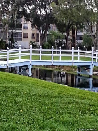 View of a small footbridge over a pond with a building in the background.