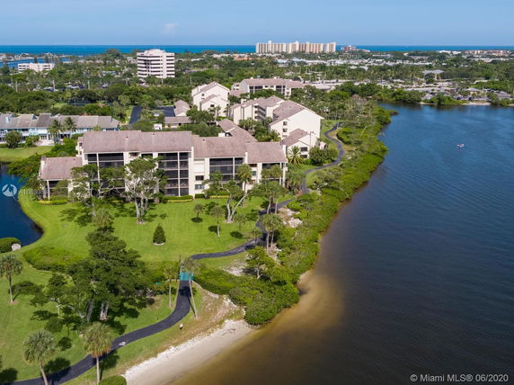 Aerial view of residential buildings near a body of water, surrounded by greenery and pathways.