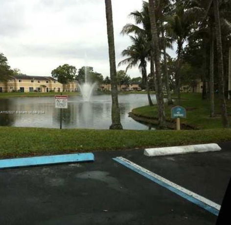 View of a fountain in a pond surrounded by palm trees and buildings.
