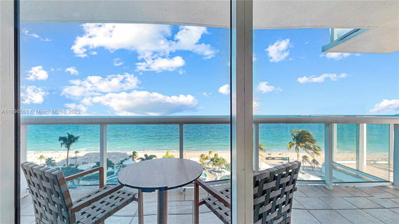 Panoramic view of the ocean from a balcony with glass railing and patio chairs.