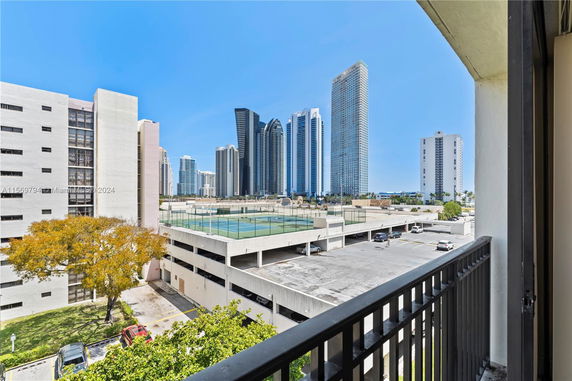 Panoramic view from a balcony overlooking a parking structure and high-rise buildings in the background.