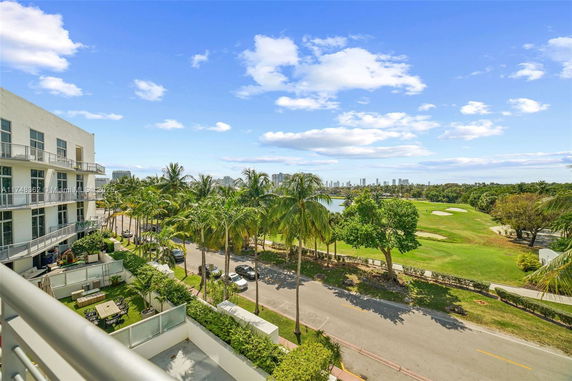 View from a building balcony overlooking a street, palm trees, and a golf course with a city skyline in the distance.