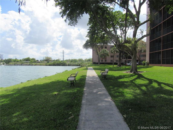 Pathway with benches alongside a water body and a building in the background.