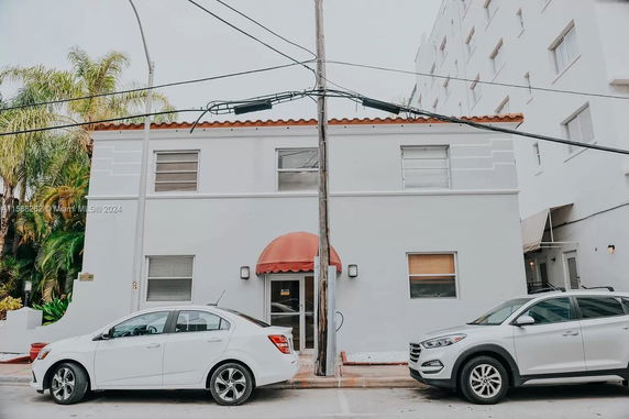 Front view of a two-story building with a red awning over the entrance and parked cars in front.