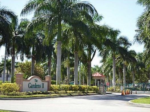 Entrance to a residential area with palm trees and a sign reading 'The Gardens II'.