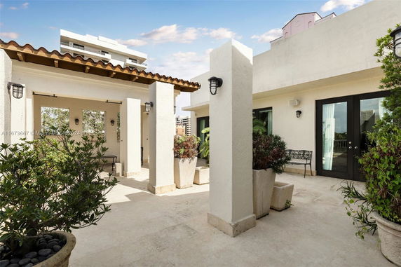 Rooftop area with potted plants and seating, featuring cream-colored walls and a tiled roof.