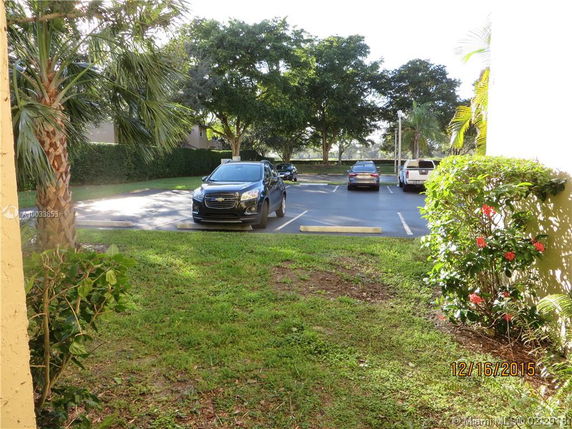 Outdoor parking area with several cars parked and surrounded by trees and shrubs.