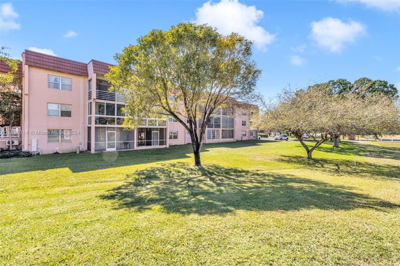 View of a multi-story residential building with surrounding green lawn and trees.