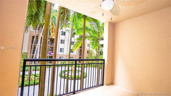 View from a balcony overlooking a courtyard with palm trees and an adjacent apartment building.