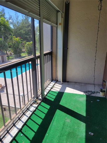 View from a balcony overlooking a swimming pool and green surroundings.