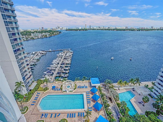 Panoramic view of a waterfront area with a swimming pool, marina, and high-rise buildings.