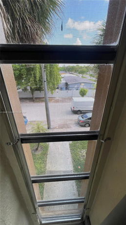 View through a window screen showing parked cars and tree-lined street.