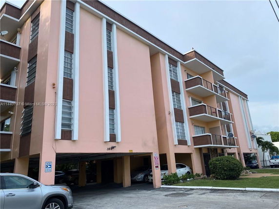 Front view of a multi-story building with balconies and parking area underneath.