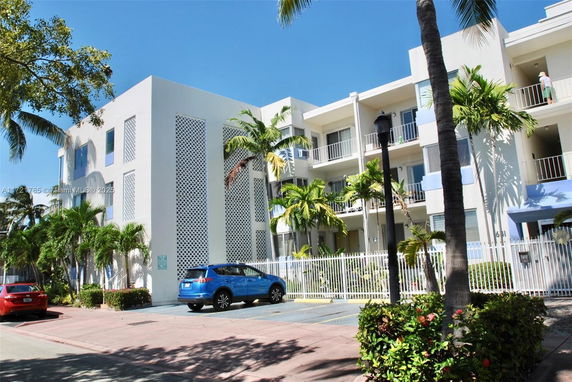 Front view of a multi-story residential building with balconies and palm trees.