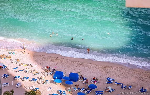 People relaxing on a sandy beach next to turquoise ocean water.