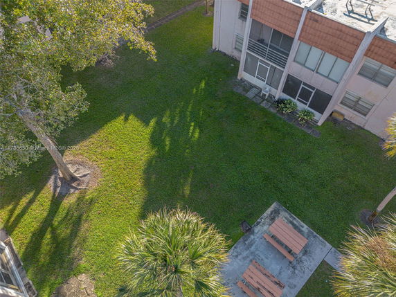 Aerial view of a green backyard area next to a building with patio benches on concrete.