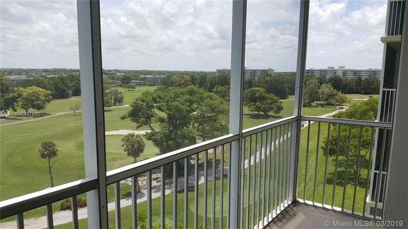 View of surrounding areas from a balcony showing expansive green fields and distant buildings.