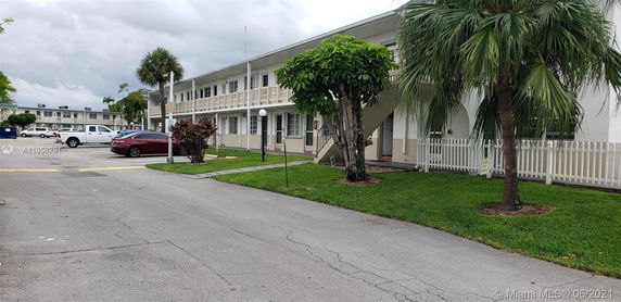 View of a two-story building with parking area and palm trees in the surroundings.