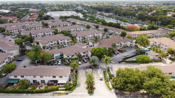 Aerial view of a residential community with multiple rows of two-story houses and parking spaces, surrounded by greenery.