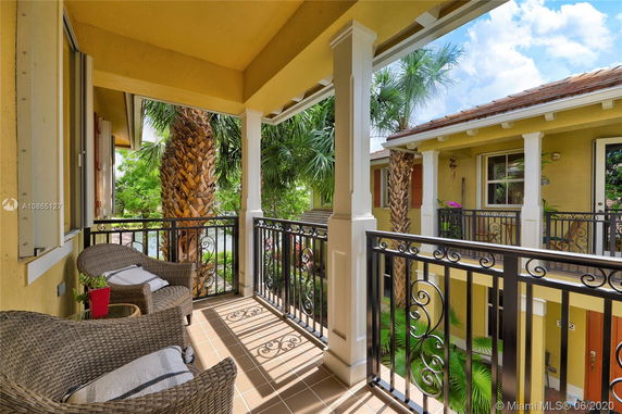 Balcony view with wicker chairs and iron railing overlooking palm trees and adjacent building.