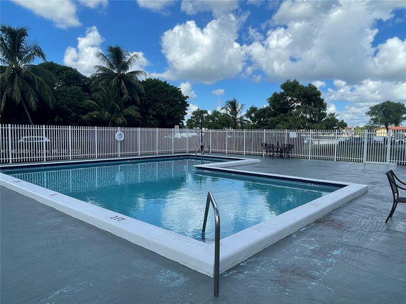 Outdoor swimming pool area with a white fence and surrounding trees.