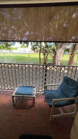 View from a patio with outdoor chairs facing a grassy area and trees.