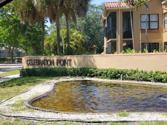 Front view of a two-story building with a sign reading 'Celebration Point' and a small pond in front.