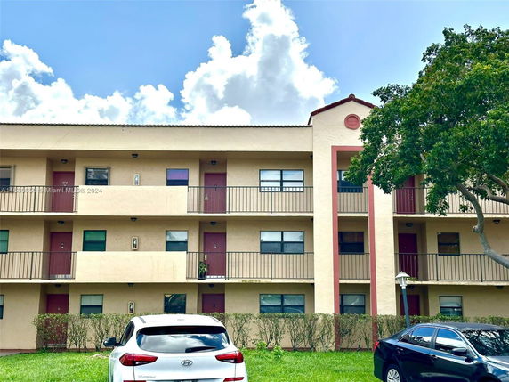 Front view of a three-story apartment building with balconies and parked cars.