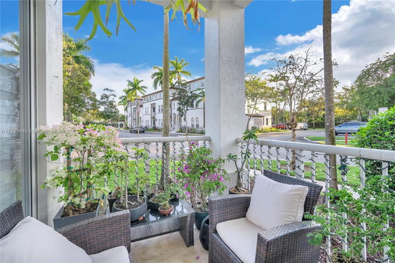 View from a porch with plants overlooking a street lined with palm trees and residential buildings.