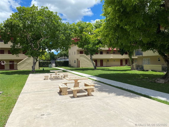 Outdoor area with benches, pathways, and residential buildings surrounded by trees.