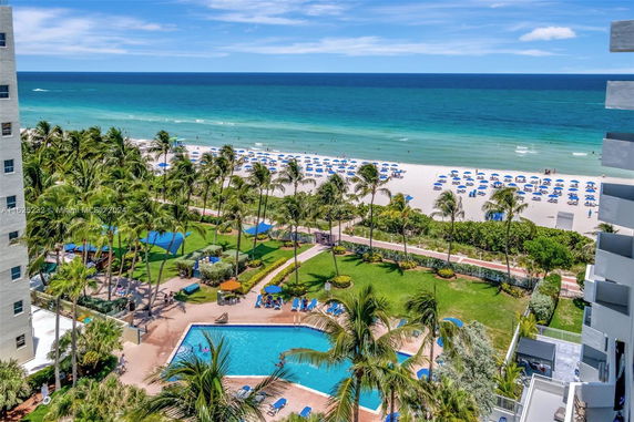 Outdoor swimming pool area near a sandy beach with palm trees and ocean view.