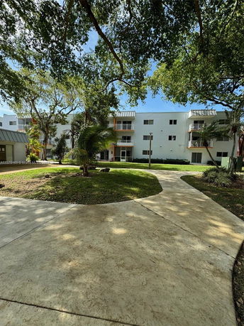 View of a multi-story residential building with balconies seen through surrounding trees.