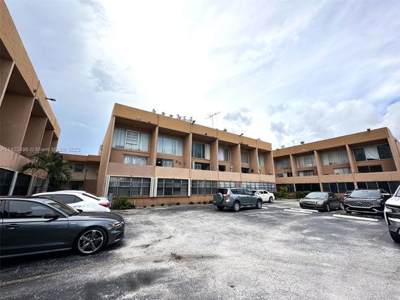 Outdoor view of a parking area with multiple cars in front of a beige multi-story building.
