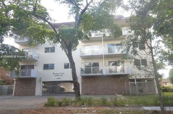 Front view of a multi-story building with balconies and gated parking area.