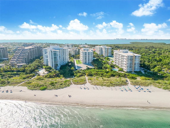 Panoramic view of beachfront residential buildings with lush greenery and a beach in the foreground.