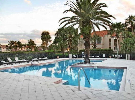 Outdoor swimming pool with palm trees and seating around the poolside.
