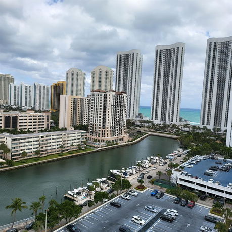 Panoramic view of tall residential buildings near a waterway and parking areas.